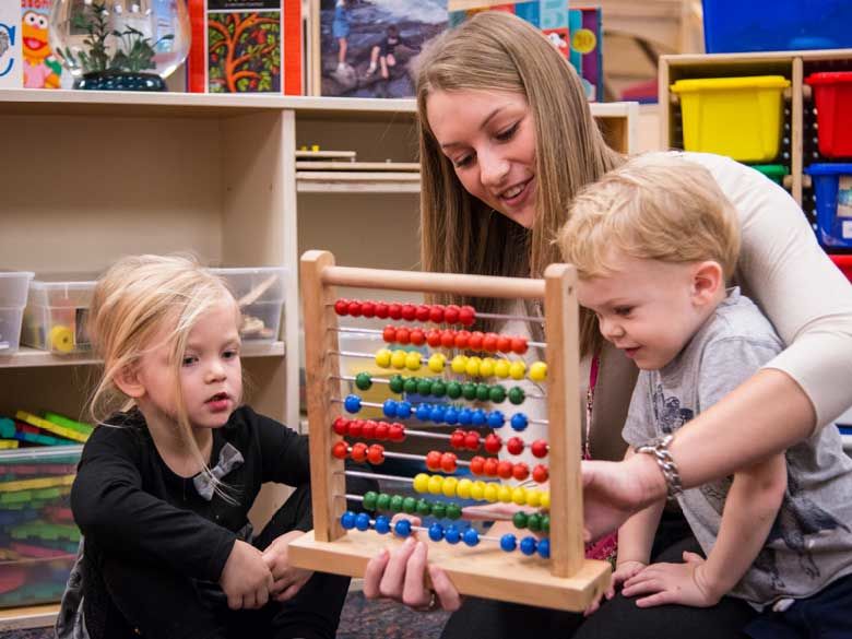 A Penn State Behrend student helps toddlers learn to count using an abacus.
